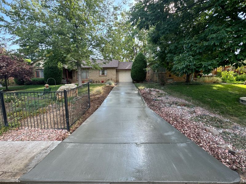 New broom-finished concrete driveway beside an iron fence at a brick ranch