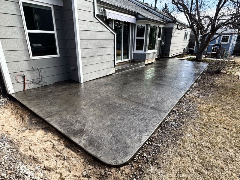 Charcoal seamless-stamped concrete patio running the full width of a back yard