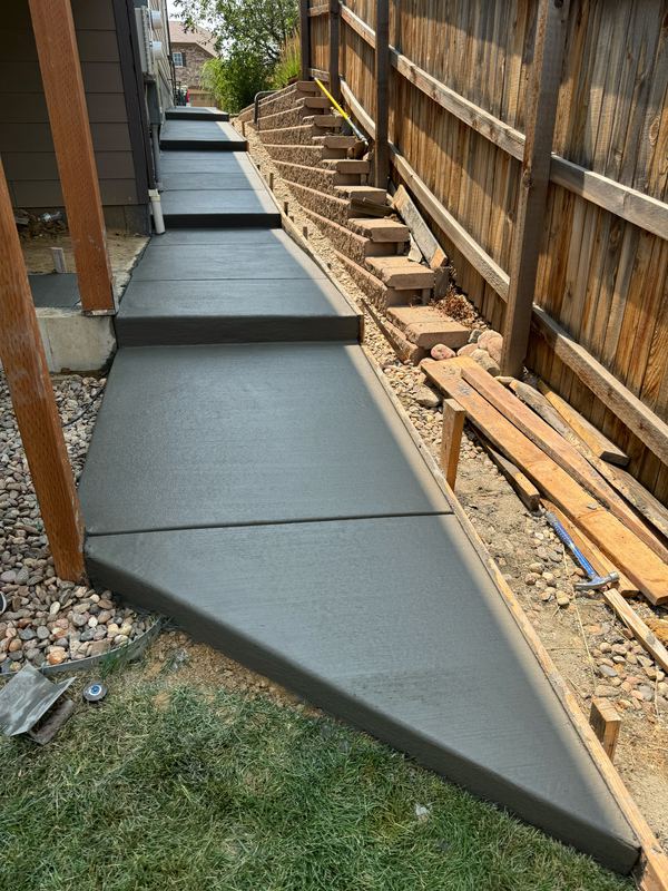 Broom-finished concrete walkway running along the side of a house to the back steps
